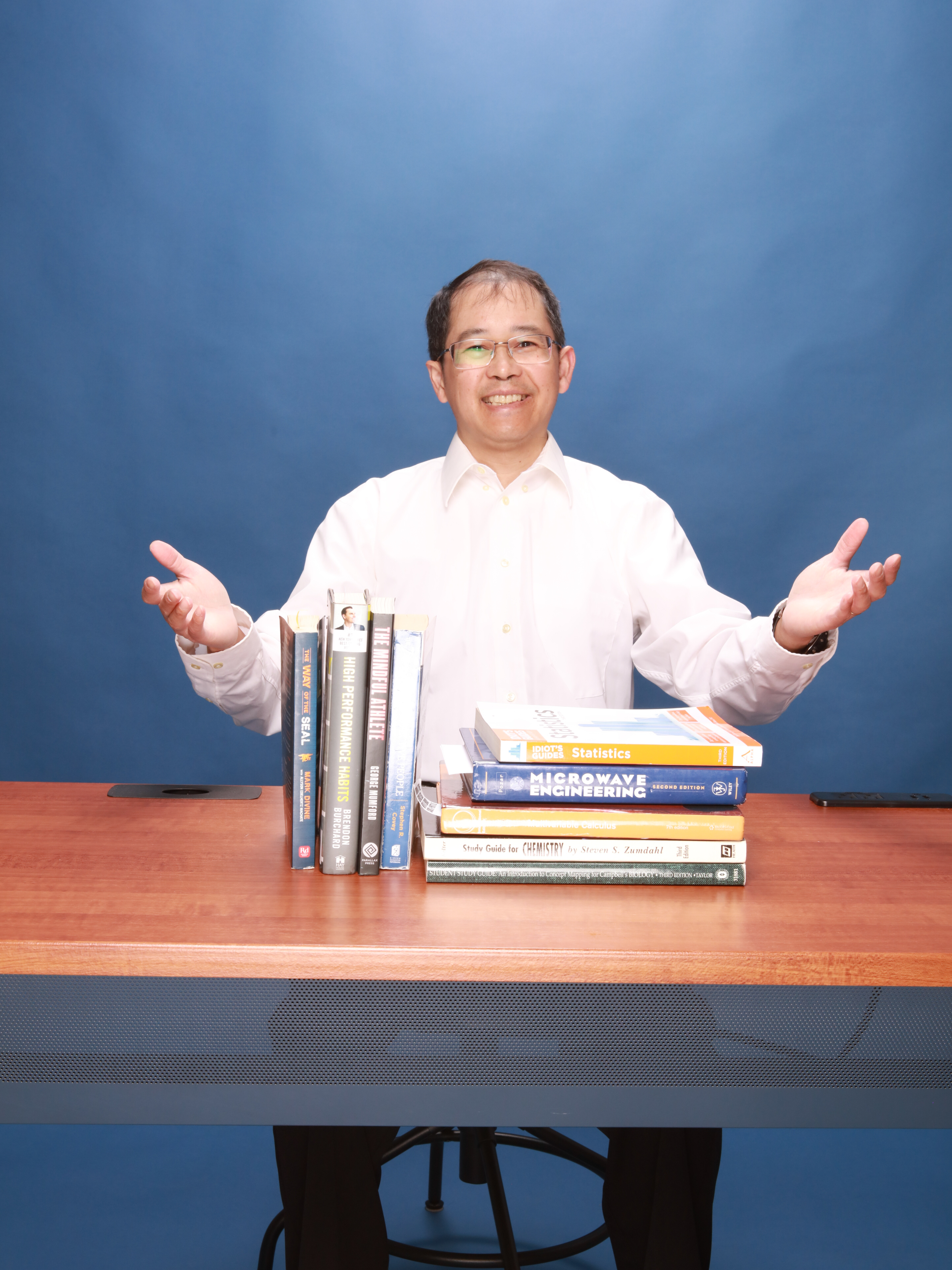 Image of Henry Nguyen with arms open in welcome, displaying some books used in tutoring and helping students succeed.