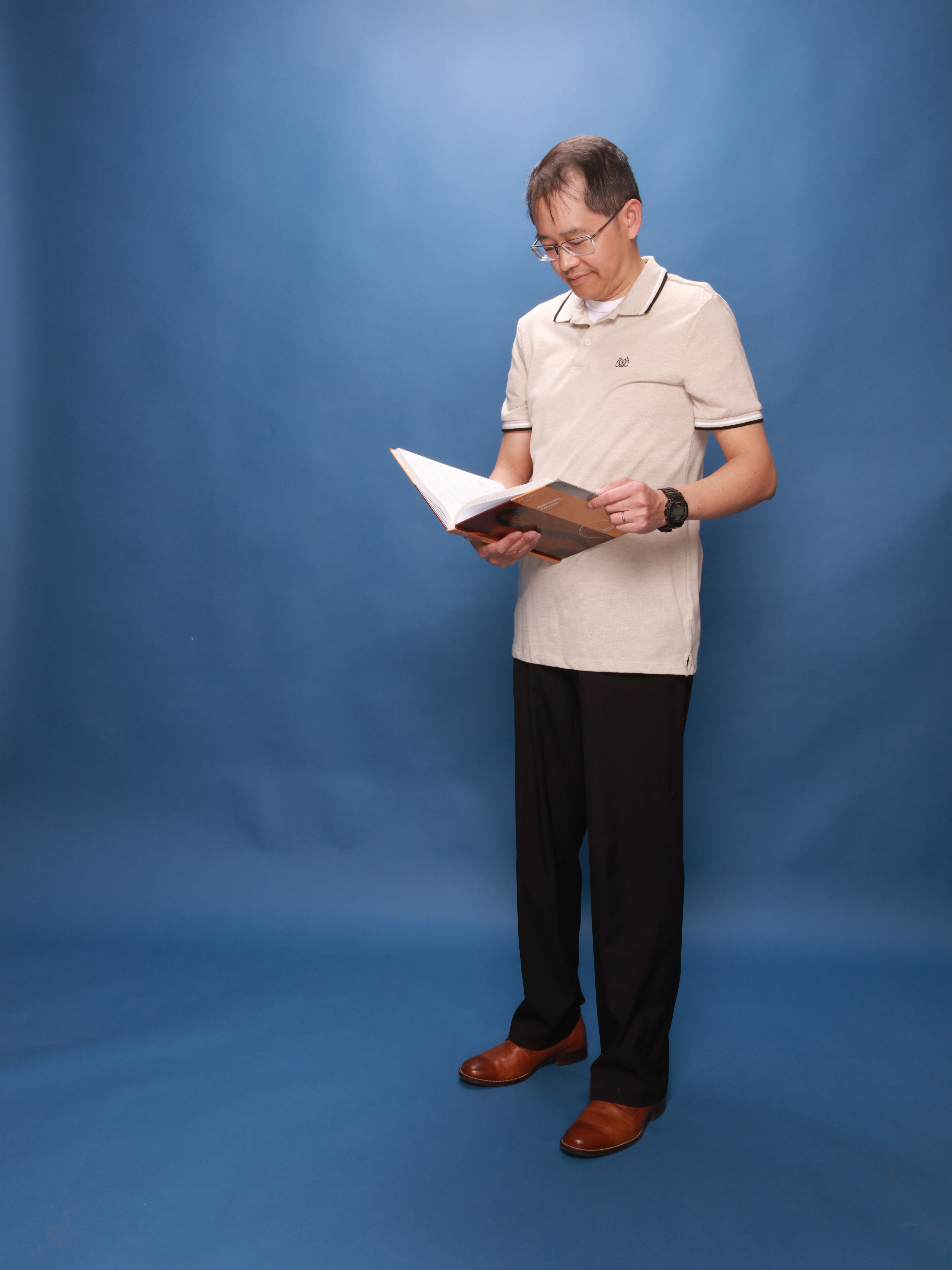 Henry Nguyen wearing a polo shirt, standing, and reading a textbook